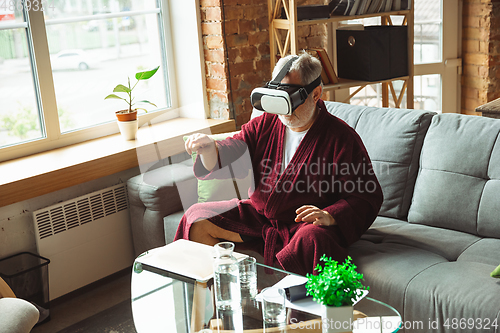 Image of Mature senior older man during quarantine, realizing how important stay at home during virus outbreak, trying on VR-headset, playing, watching