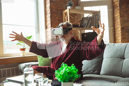 Image of Mature senior older man during quarantine, realizing how important stay at home during virus outbreak, trying on VR-headset, playing, watching