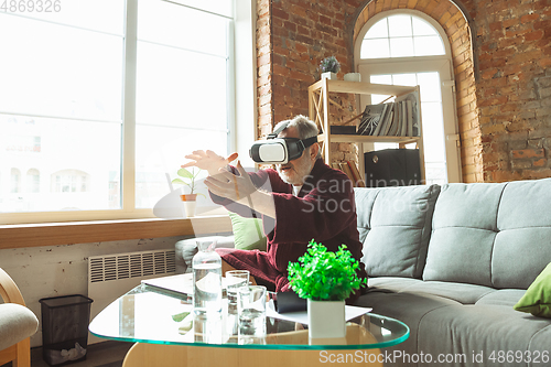 Image of Mature senior older man during quarantine, realizing how important stay at home during virus outbreak, trying on VR-headset, playing, watching