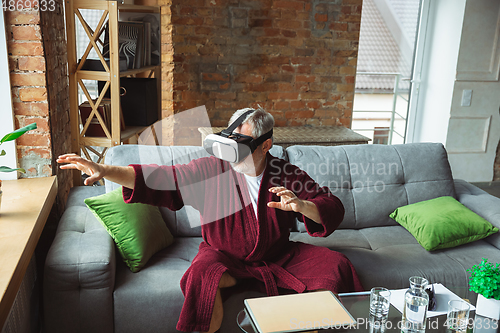 Image of Mature senior older man during quarantine, realizing how important stay at home during virus outbreak, trying on VR-headset, playing, watching