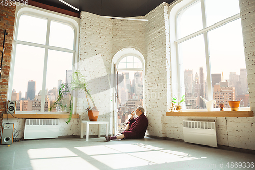 Image of Mature senior older man during quarantine, realizing how important stay at home during virus outbreak, looking throught window on day New York city