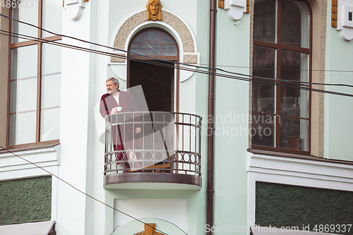 Image of Mature senior older man during quarantine, realizing how important stay at home during virus outbreak, drinking coffee on the balcony