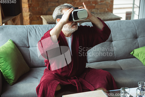 Image of Mature senior older man during quarantine, realizing how important stay at home during virus outbreak, trying on VR-headset, playing, watching