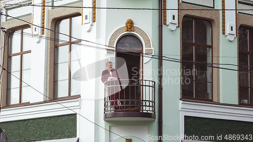 Image of Mature senior older man during quarantine, realizing how important stay at home during virus outbreak, drinking coffee on the balcony