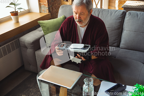 Image of Mature senior older man during quarantine, realizing how important stay at home during virus outbreak, trying on VR-headset, playing, watching