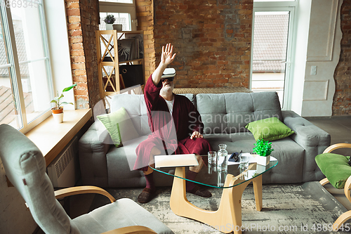 Image of Mature senior older man during quarantine, realizing how important stay at home during virus outbreak, trying on VR-headset, playing, watching