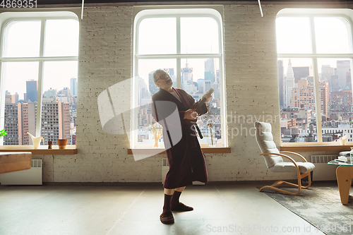 Image of Mature senior older man during quarantine, realizing how important stay at home during virus outbreak, giving concert of taking online lessons of guitar playing in USA