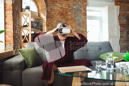 Image of Mature senior older man during quarantine, realizing how important stay at home during virus outbreak, trying on VR-headset, playing, watching