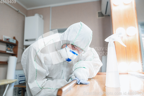 Image of Coronavirus Pandemic. A disinfector in a protective suit and mask sprays disinfectants in the house or office