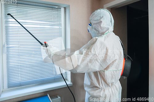 Image of Coronavirus Pandemic. A disinfector in a protective suit and mask sprays disinfectants in the house or office