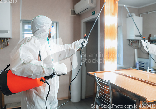 Image of Coronavirus Pandemic. A disinfector in a protective suit and mask sprays disinfectants in the house or office