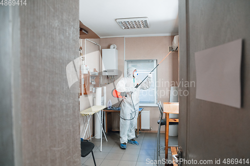 Image of Coronavirus Pandemic. A disinfector in a protective suit and mask sprays disinfectants in the house or office