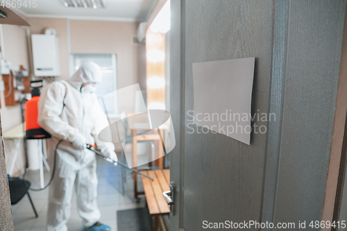 Image of Coronavirus Pandemic. A disinfector in a protective suit and mask sprays disinfectants in the house or office