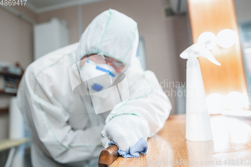 Image of Coronavirus Pandemic. A disinfector in a protective suit and mask sprays disinfectants in the house or office