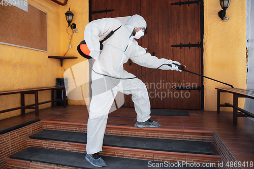 Image of Coronavirus Pandemic. A disinfector in a protective suit and mask sprays disinfectants in the house or office