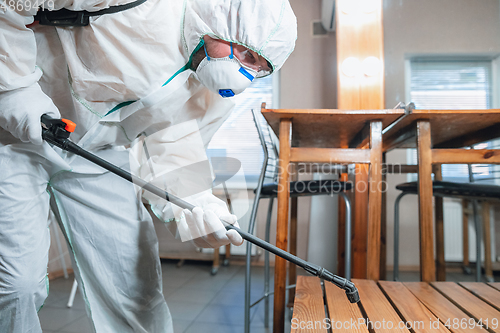 Image of Coronavirus Pandemic. A disinfector in a protective suit and mask sprays disinfectants in the house or office