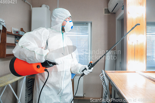 Image of Coronavirus Pandemic. A disinfector in a protective suit and mask sprays disinfectants in the house or office