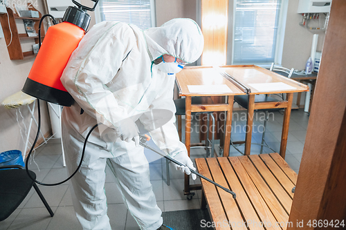 Image of Coronavirus Pandemic. A disinfector in a protective suit and mask sprays disinfectants in the house or office