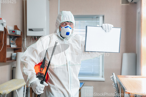 Image of Coronavirus Pandemic. A disinfector in a protective suit and mask sprays disinfectants in the house or office