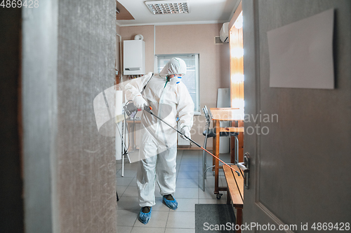 Image of Coronavirus Pandemic. A disinfector in a protective suit and mask sprays disinfectants in the house or office