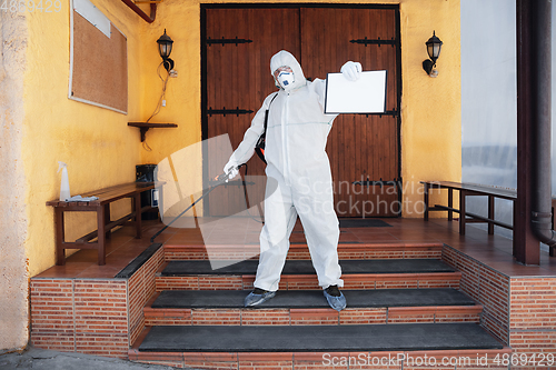 Image of Coronavirus Pandemic. A disinfector in a protective suit and mask sprays disinfectants in the house or office