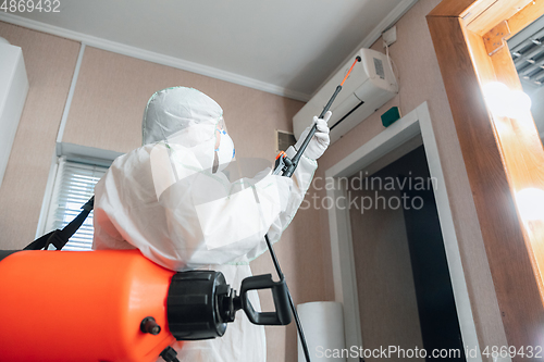 Image of Coronavirus Pandemic. A disinfector in a protective suit and mask sprays disinfectants in the house or office