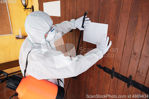 Image of Coronavirus Pandemic. A disinfector in a protective suit and mask sprays disinfectants in the house or office