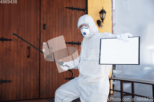 Image of Coronavirus Pandemic. A disinfector in a protective suit and mask sprays disinfectants in the house or office