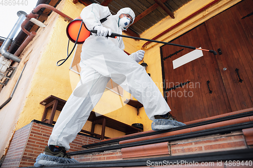 Image of Coronavirus Pandemic. A disinfector in a protective suit and mask sprays disinfectants in the house or office