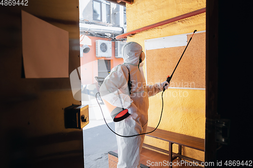 Image of Coronavirus Pandemic. A disinfector in a protective suit and mask sprays disinfectants in the house or office