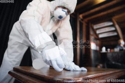 Image of Coronavirus Pandemic. A disinfector in a protective suit and mask sprays disinfectants in the house or office