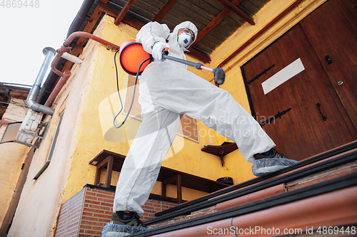 Image of Coronavirus Pandemic. A disinfector in a protective suit and mask sprays disinfectants in the house or office