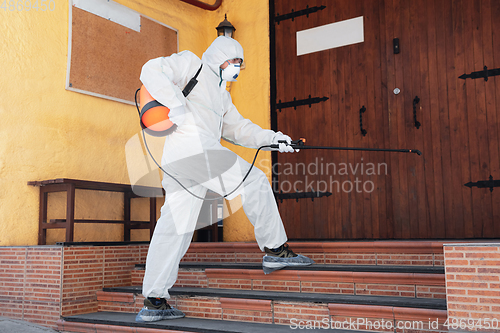 Image of Coronavirus Pandemic. A disinfector in a protective suit and mask sprays disinfectants in the house or office