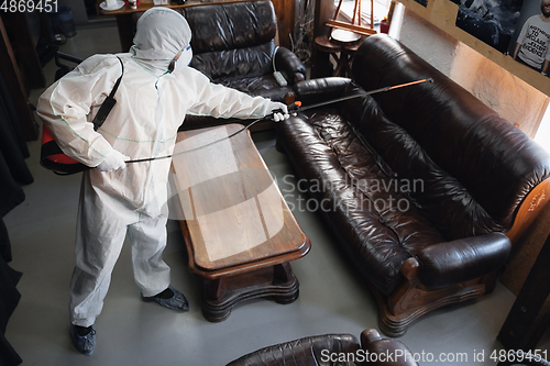 Image of Coronavirus Pandemic. A disinfector in a protective suit and mask sprays disinfectants in the house or office