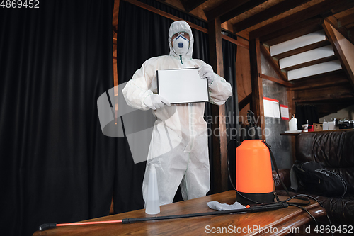 Image of Coronavirus Pandemic. A disinfector in a protective suit and mask sprays disinfectants in the house or office