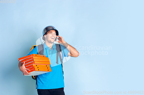 Image of Contacless delivery service during quarantine. Man delivers food and shopping bags during insulation. Emotions of deliveryman isolated on blue background.