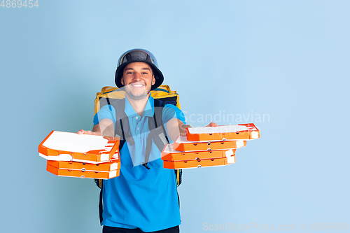 Image of Contacless delivery service during quarantine. Man delivers food and shopping bags during insulation. Emotions of deliveryman isolated on blue background.