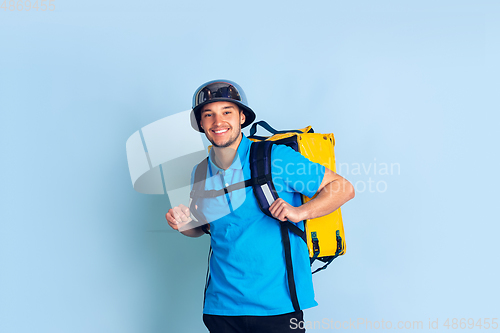 Image of Contacless delivery service during quarantine. Man delivers food and shopping bags during insulation. Emotions of deliveryman isolated on blue background.