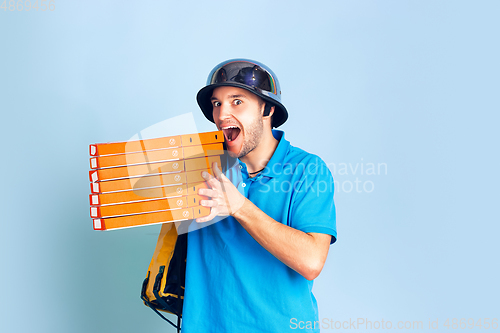 Image of Contacless delivery service during quarantine. Man delivers food and shopping bags during insulation. Emotions of deliveryman isolated on blue background.