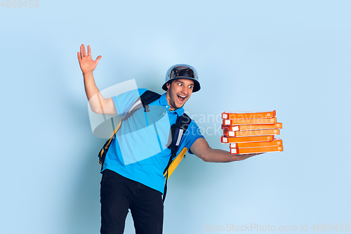 Image of Contacless delivery service during quarantine. Man delivers food and shopping bags during insulation. Emotions of deliveryman isolated on blue background.