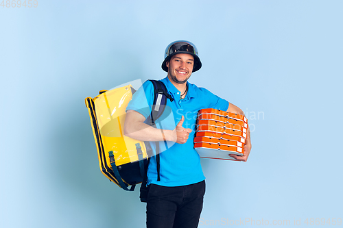 Image of Contacless delivery service during quarantine. Man delivers food and shopping bags during insulation. Emotions of deliveryman isolated on blue background.