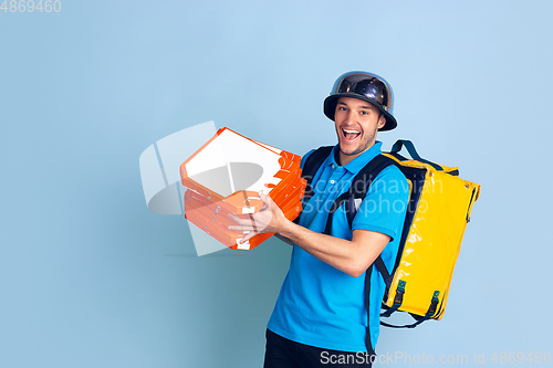 Image of Contacless delivery service during quarantine. Man delivers food and shopping bags during insulation. Emotions of deliveryman isolated on blue background.