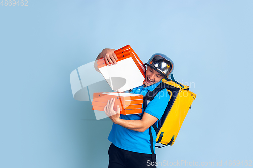 Image of Contacless delivery service during quarantine. Man delivers food and shopping bags during insulation. Emotions of deliveryman isolated on blue background.