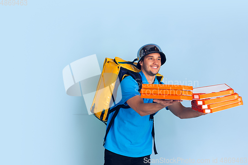 Image of Contacless delivery service during quarantine. Man delivers food and shopping bags during insulation. Emotions of deliveryman isolated on blue background.