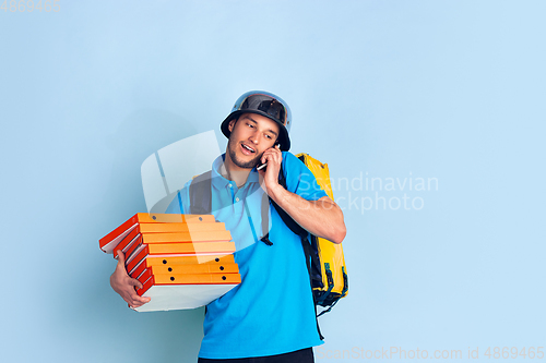 Image of Contacless delivery service during quarantine. Man delivers food and shopping bags during insulation. Emotions of deliveryman isolated on blue background.