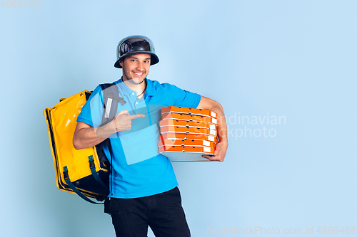 Image of Contacless delivery service during quarantine. Man delivers food and shopping bags during insulation. Emotions of deliveryman isolated on blue background.