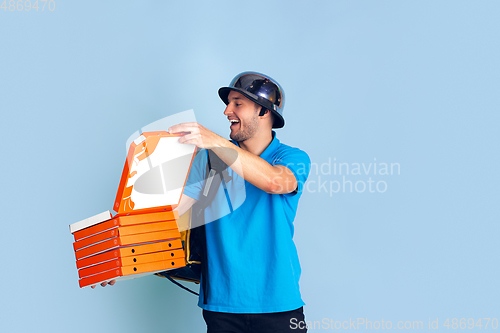 Image of Contacless delivery service during quarantine. Man delivers food and shopping bags during insulation. Emotions of deliveryman isolated on blue background.