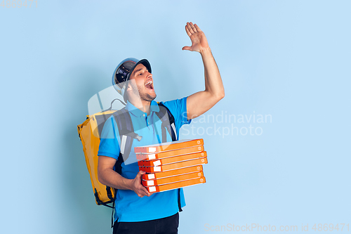 Image of Contacless delivery service during quarantine. Man delivers food and shopping bags during insulation. Emotions of deliveryman isolated on blue background.