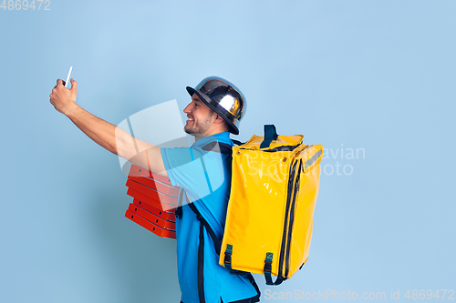 Image of Contacless delivery service during quarantine. Man delivers food and shopping bags during insulation. Emotions of deliveryman isolated on blue background.