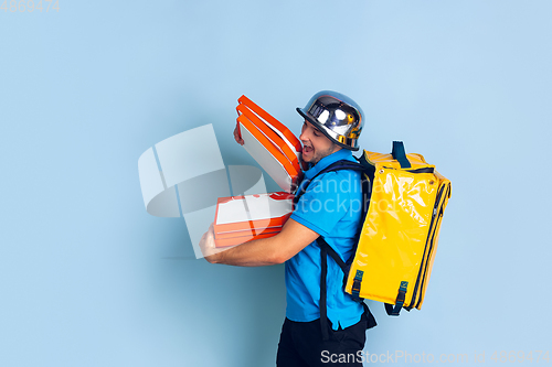 Image of Contacless delivery service during quarantine. Man delivers food and shopping bags during insulation. Emotions of deliveryman isolated on blue background.
